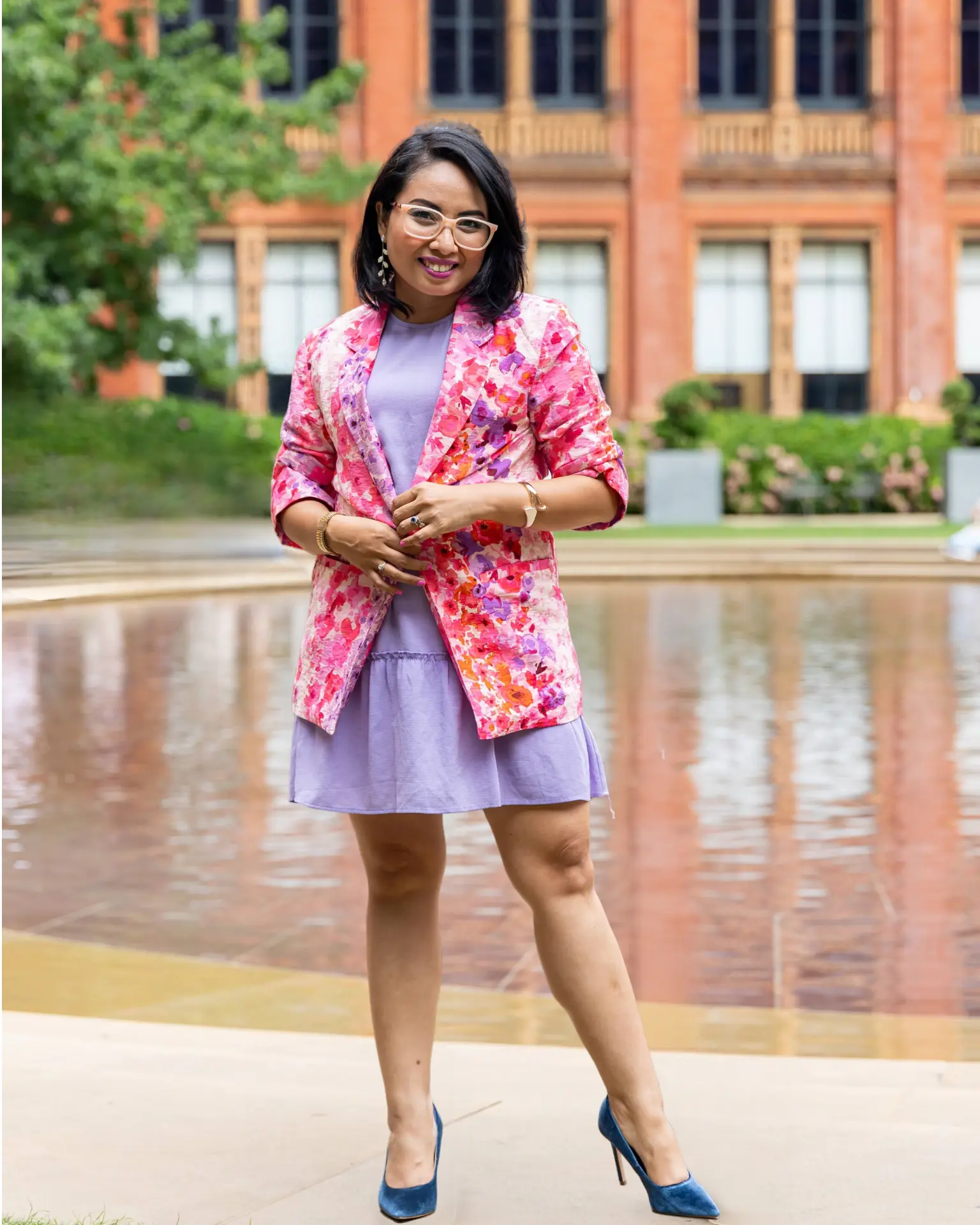 Rebecca Leppard in a floral pink jacket and lilac dress beside a reflecting pool